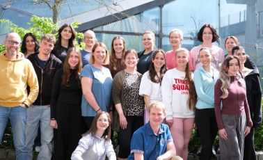 Man sieht 22 Männer und Frauen auf dem Gruppenbild, die bei sonnenschein in die Kamera gucken und sich freuen.
