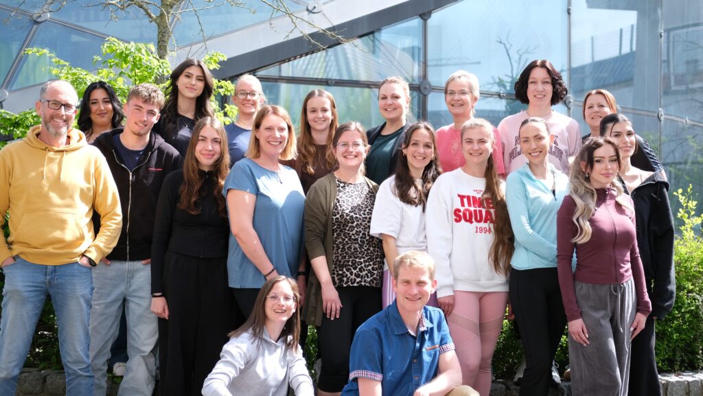 Man sieht 22 Männer und Frauen auf dem Gruppenbild, die bei sonnenschein in die Kamera gucken und sich freuen.